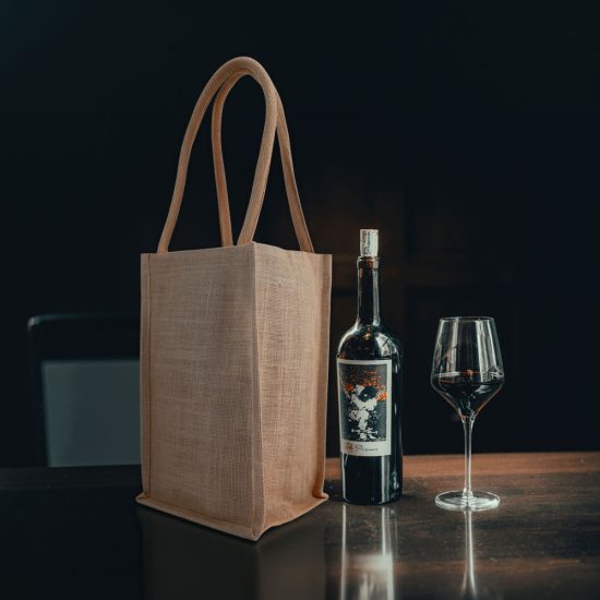 Four bottle wine carrier jute bag on a table next to a bottle of wine.